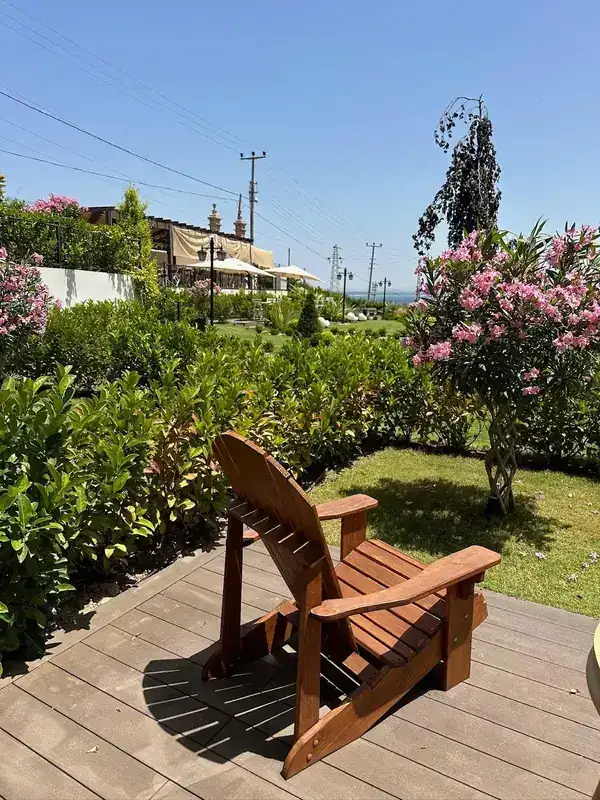 Bahçedeki ahşap terasta sandalye ve çiçek açmış zakkumlar